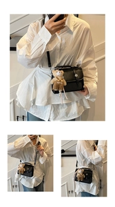 Detail of black PU leather crossbody bag with metal lock, rivet decor and plush bear charm