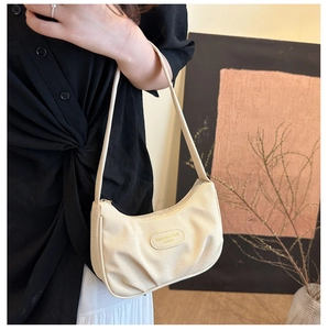 Vista laterale della modella con borsa sottobraccio in tela beige a forma di mezzaluna