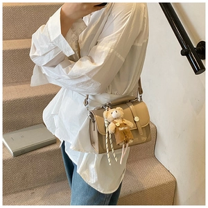 Detail of beige square crossbody bag with metallic buckle and cute bear pendant