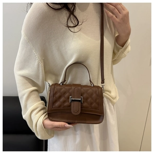 Détail de la texture en cuir matelassé et de la boucle en métal d'un sac brun