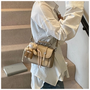 Detail of crossbody bag with beige texture patchwork and a cute teddy bear charm