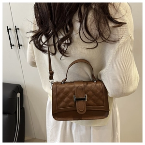 Close-up of brown quilted faux leather handbag with metal buckle and shoulder strap