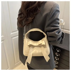 Detail of a creamy white dumpling bag with an elegant oversized bow and metal chain