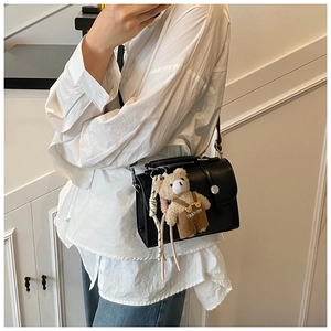 Detail of black crossbody square bag with silver lock and a cute plush bear pendant
