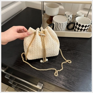 Detail of straw bucket bag featuring gold chain strap and elegant pearl drawstrings