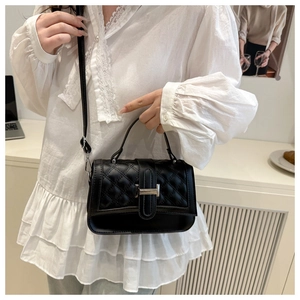 Gros plan du sac bandoulière matelassé noir avec boucle argentée porté par un mannequin