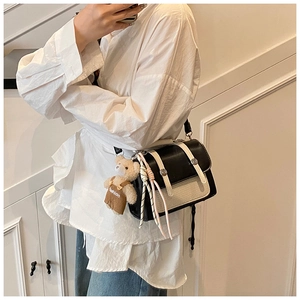Detail of chic black leather crossbody bag with woven cream flap and plush bear charm