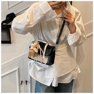 Detail of a chic black and beige crossbody bag with a cute plush bear charm accessory