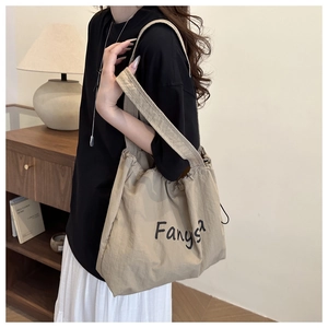 Detail of khaki nylon drawstring tote bag with letter print in minimalist home setting