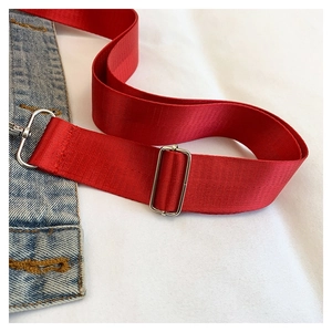 Dettaglio della tracolla in nylon rosso con gancio in metallo su borsa di denim