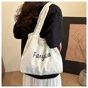 Nahaufnahme der weißen Canvas-Tasche mit Kordelzug, schwarzem Fanyssa-Schriftzug und Riemen