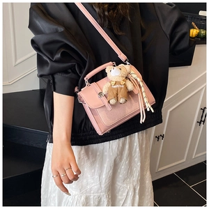 Detail view of pink leather crossbody bag with mesh texture and cute teddy bear charm