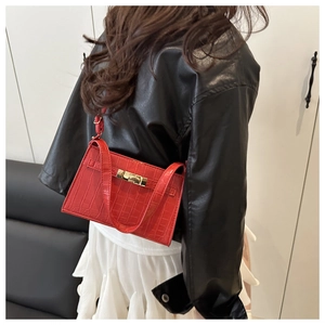 Close-up of red crocodile embossed handbag with golden clasp worn by a model