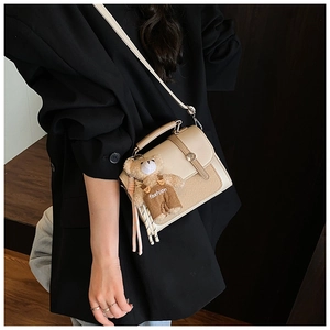 Detail of beige woven crossbody bag with metal buckle and plush bear charm