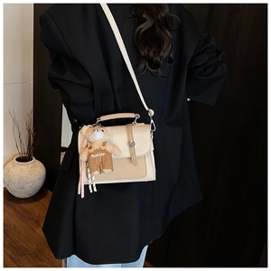 Detail of beige crossbody bag with woven texture, metal buckle and cute bear charm