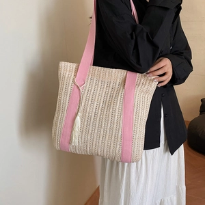 Handwoven straw tote bag with pink fabric straps and white tassel charm on shoulder