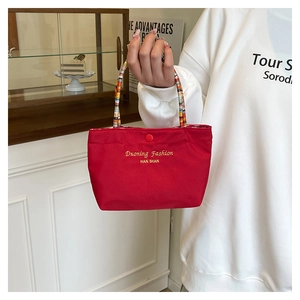 Detail der roten Canvas-Handtasche mit buntem Webgriff und goldener Logostickerei