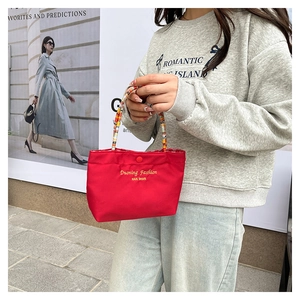 Close-up of red nylon tote bag with colorful woven handle and yellow brand embroidery