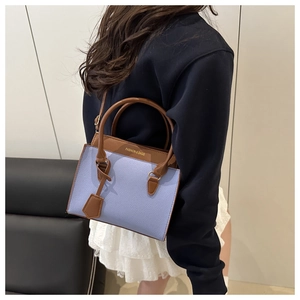 Detail of lilac and brown leather handbag showing textured finish and golden logo