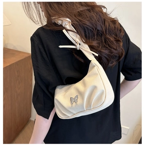 Close-up of pleated beige canvas shoulder bag with silver butterfly emblem on a model