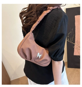 Detail view of brown pleated baguette bag with white butterfly metal accessory