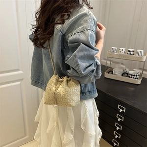 Straw drawstring bucket bag with gold chain and pearl charm detail worn over the shoulder