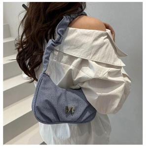 Détail du sac à bandoulière en denim bleu avec boucle papillon argentée et sangle plissée