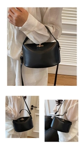 Detail view of black leather semi-circular bag with gold metal rotating lock and strap
