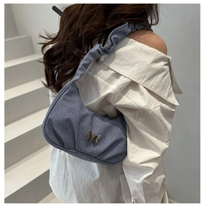 Détail du sac croissant en denim bleu avec boucle papillon porté sur l'épaule
