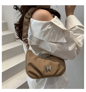 Détail d'un sac sous les aisselles en tissu marron avec boucle papillon et bandoulière plissée