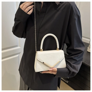Detail of white glitter handbag with gold V-shaped buckle and chain strap on black shirt