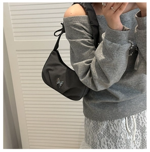 Détail du sac hobo plissé noir avec logo papillon argenté sur une bandoulière textile