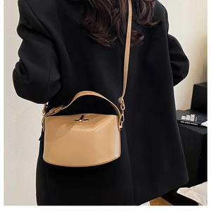 Detail of khaki leather bucket bag with gold buckle worn on a black blazer by model
