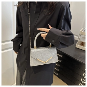 Detail of silver sequined handbag featuring a V-shaped gold metal trim and chain strap