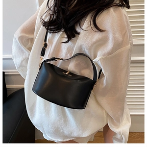 Detail einer mattschwarzen Lederhandtasche mit goldener Schnalle an einem Modell in Weiß