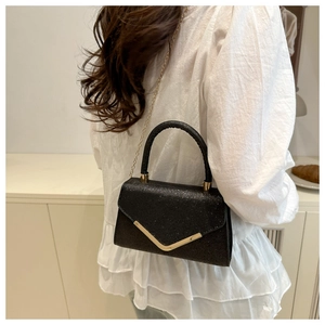 Detail of black glitter handbag featuring a gold V-shaped metal clasp and chain strap
