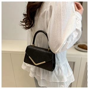 Detail of elegant black glitter handbag with gold V-metal decor on white shirt