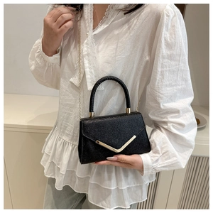 Detail of black glitter handbag featuring gold V-shaped buckle and slim chain strap