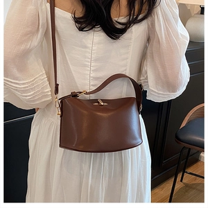 Detail of dark brown leather bucket bag with gold clasp shown on a model