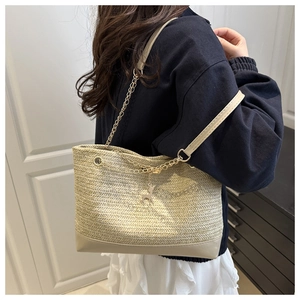 Detail of straw woven tote bag featuring white leather base and silver deer pendant charm