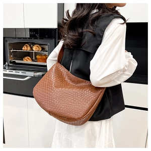Rear view of a textured woven brown leather hobo bag worn over the shoulder by a model