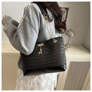 Detail of black woven straw tote bag with gold chain strap and deer charm pendant