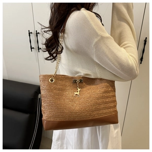 Detail of woven straw tote with leather base, chain strap and deer charm on shoulder