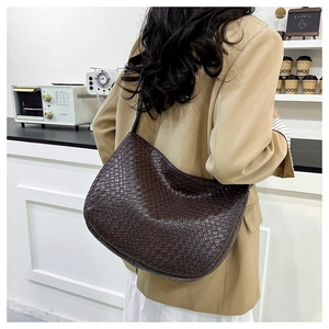 Detailed view of dark brown woven leather hobo bag worn by a model in a cafe setting