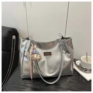 Detail of silver metallic tote bag with chain strap and plush monkey charm on desk