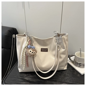 Close-up of beige tote bag with silver chain strap and brown logo patch on wooden desk