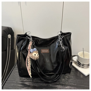 Detail of glossy black tote bag with metal chain handles and plush bear pendant accessory