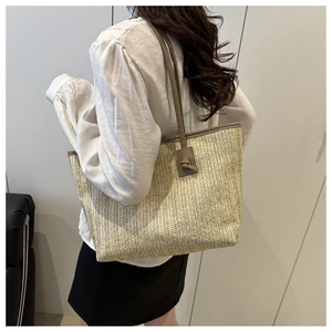 Detailed close-up of woven beige straw tote bag with knotted brown leather straps