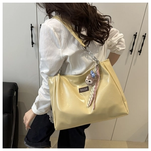 Detail view of a yellow large capacity tote bag with metal chain strap and plush pendant