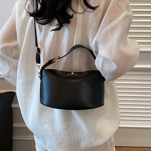 Minimalistische schwarze Umhängetasche mit goldener Hardware an einem Modell in Weiß